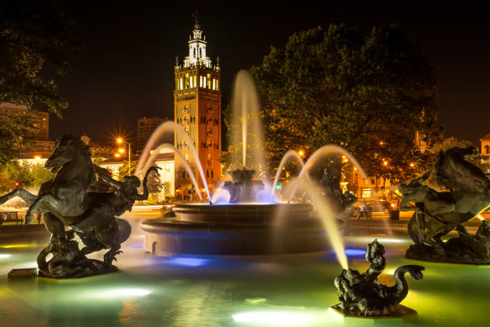Nighttime shot of decorative fountain with horses and Country Club Plaza tower in background